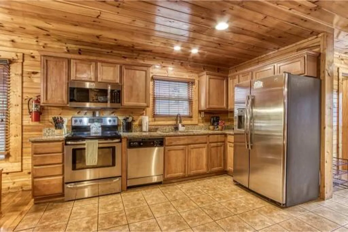 A luxurious kitchen featuring stainless steel appliances, gleaming granite countertops, rich wood cabinetry, and tile flooring. The space radiates warmth and is clearly designed for cooking, entertaining, and gathering with family and friends.