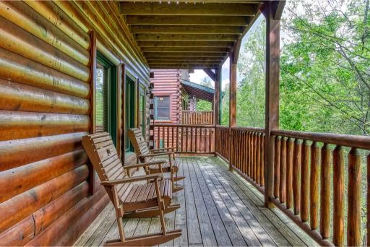 This exterior scene features classic log cabin walls, wooden railings, and a set of inviting rocking chairs overlooking lush greenery. The space exudes relaxation, offering guests a spot to unwind and soak in the natural surroundings after a day of exploring art and culture in town.