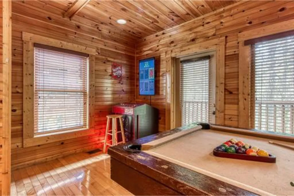 A vibrant, playful game room scene with a pool table set up for a game, a classic arcade machine in the background, a bar stool, and colorful pool balls. The wood-paneled backdrop and ample lighting create an energetic atmosphere ideal for social gatherings and friendly competition.