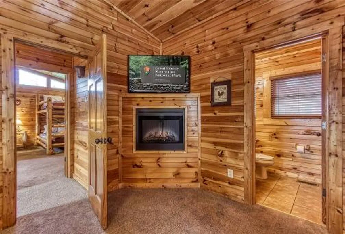 This inviting space showcases a rustic stone fireplace, a flat-screen TV, and rich wood paneling, with open doors that hint at flowing movement between spaces. The furnishings, textures, and lighting evoke both warmth and luxury, perfect for memorable family moments.