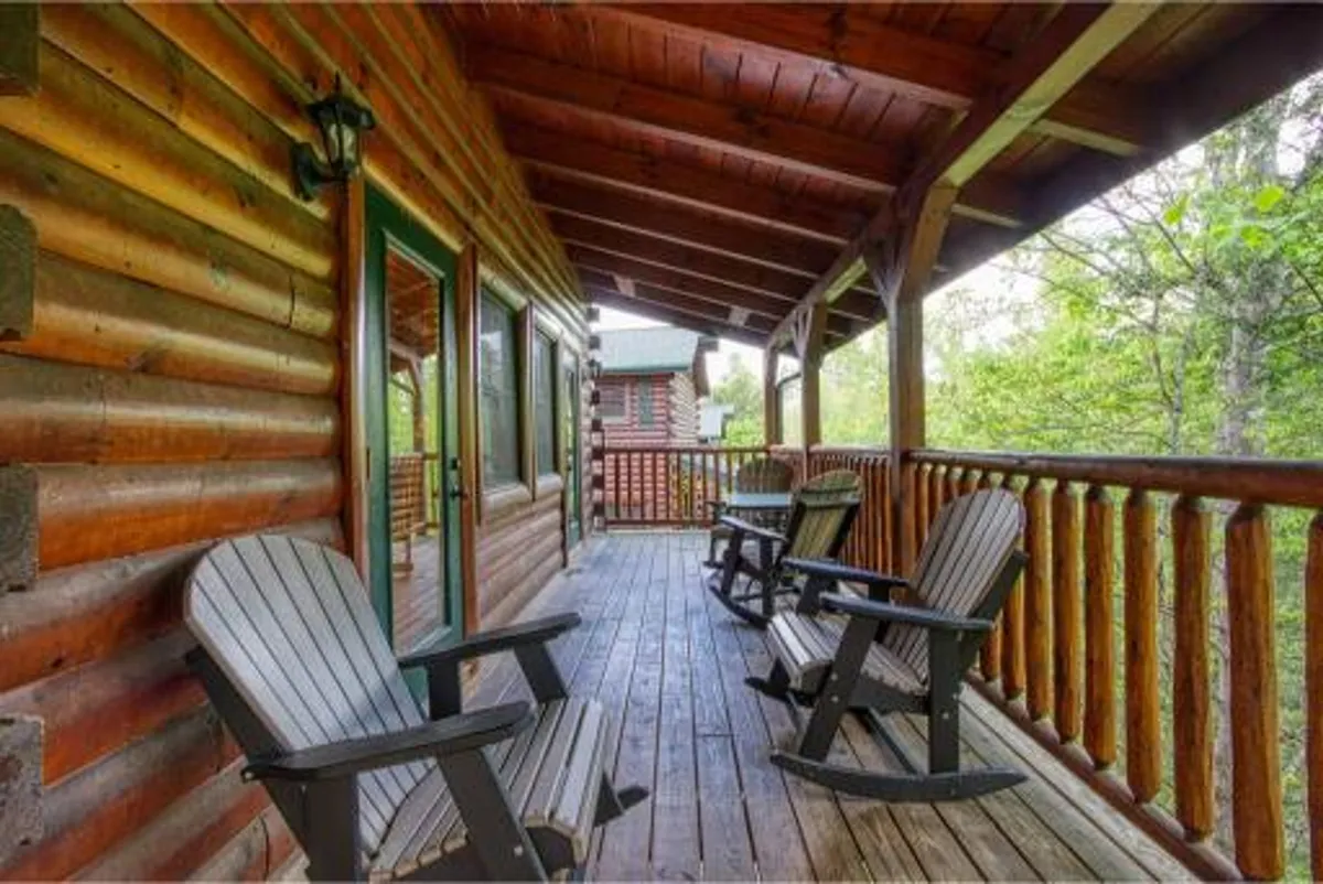 A welcoming exterior view of the log cabin showing wooden rocking chairs on the porch, surrounded by lush greenery. The scene reflects tranquility and an inviting space to unwind, perhaps after an adventurous day outdoors.