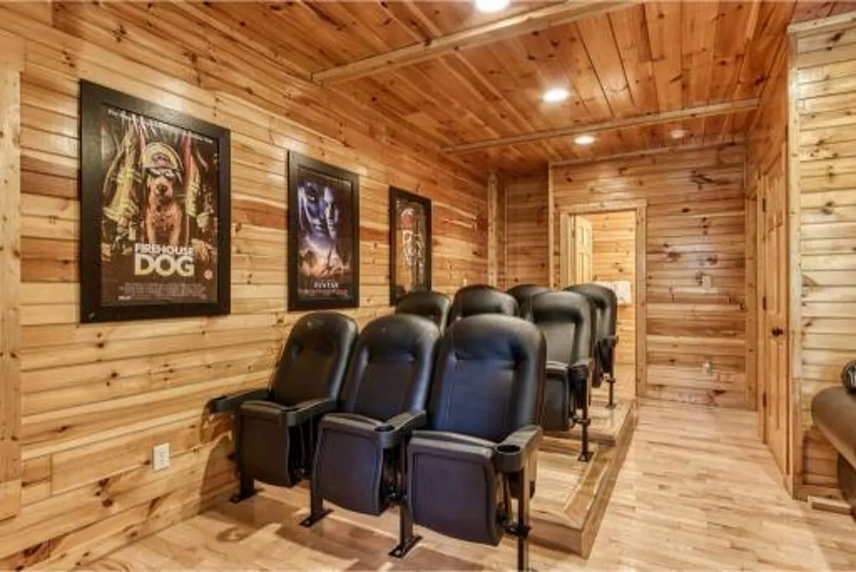 A dedicated home theater space with rows of plush black leather reclining chairs, movie posters adorning the wood-paneled walls, and a dim, cinematic ambiance. The seating arrangement is designed for optimal comfort and an immersive viewing experience.