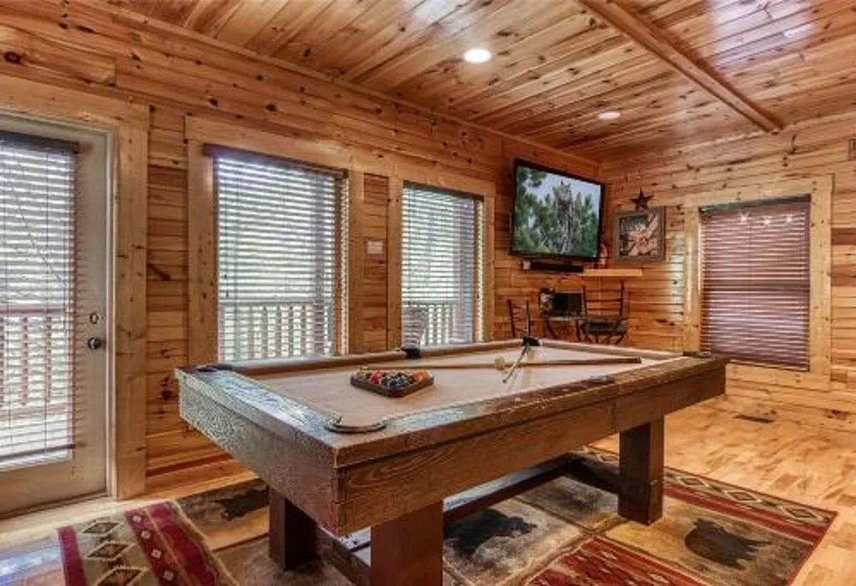 A lively interior game room featuring a pool table, television, wooden walls, and a rug. The space exudes a friendly, communal atmosphere ideal for post-adventure game nights and group entertainment.