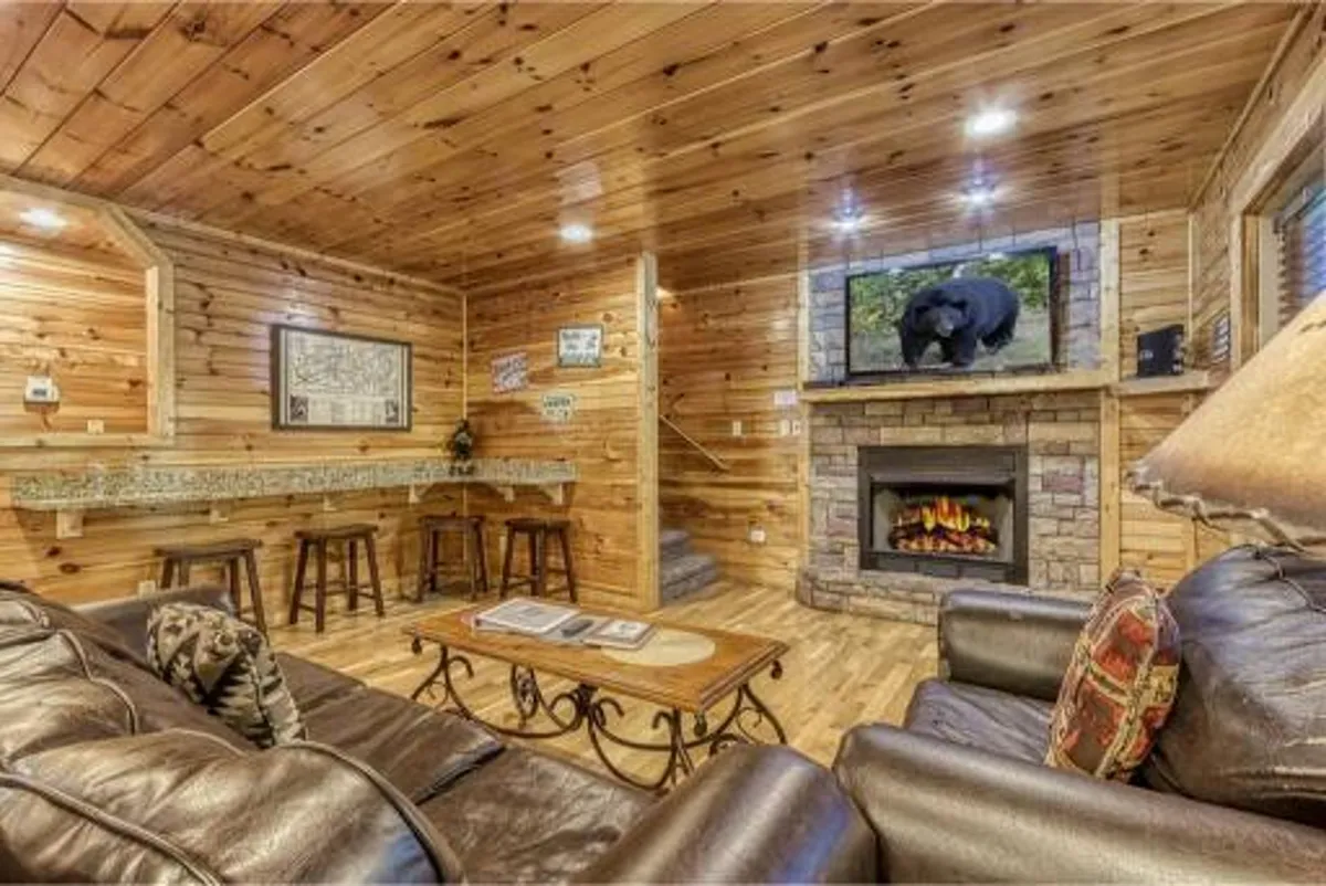 A comfortable living area centered around a fireplace, with a sofa, television, and a stylish bar area. Natural wood tones and soft lighting create a cozy, inviting space ideal for relaxing, entertaining, or hosting friends and family.